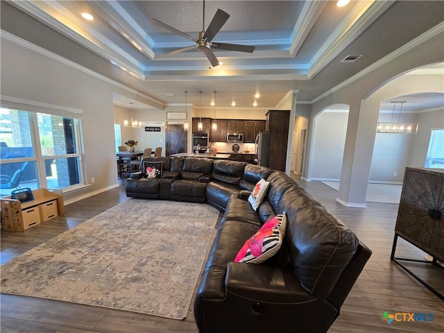 living room with a raised ceiling, arched walkways, plenty of natural light, and ceiling fan with notable chandelier