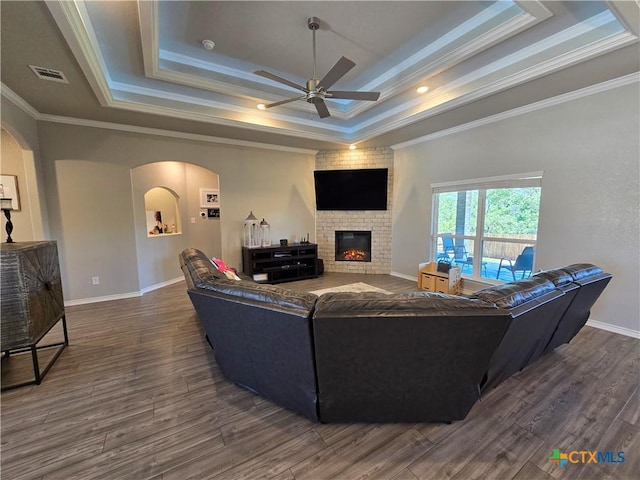 living room with a raised ceiling, ceiling fan, arched walkways, dark wood-style flooring, and ornamental molding