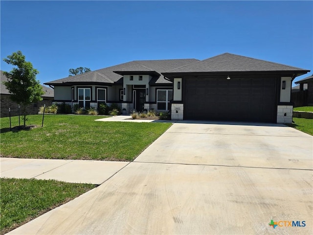 prairie-style home featuring a garage, roof with shingles, concrete driveway, and a front lawn