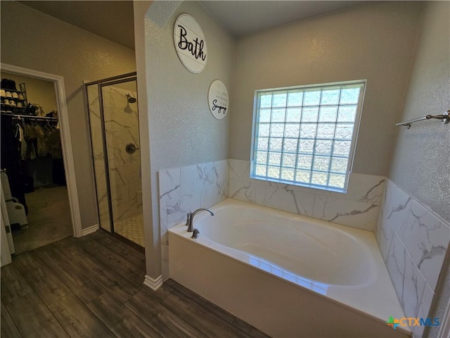 full bath featuring a textured wall, a stall shower, a garden tub, a walk in closet, and wood finished floors
