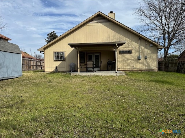 rear view of property with a lawn, a fenced backyard, a chimney, an outdoor structure, and a patio area