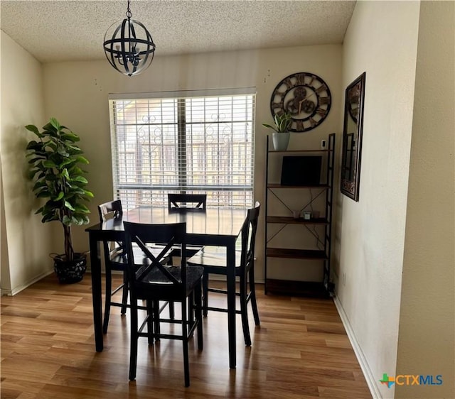 dining room with a notable chandelier, a textured ceiling, baseboards, and wood finished floors