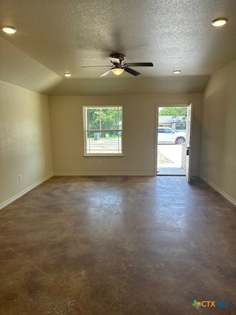 carpeted empty room featuring a textured ceiling, lofted ceiling, a healthy amount of sunlight, and ceiling fan