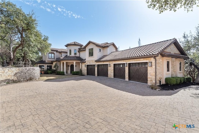 mediterranean / spanish home featuring decorative driveway, stone siding, a tiled roof, and stucco siding