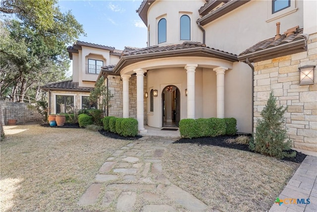 property entrance with stone siding, fence, a tiled roof, and stucco siding