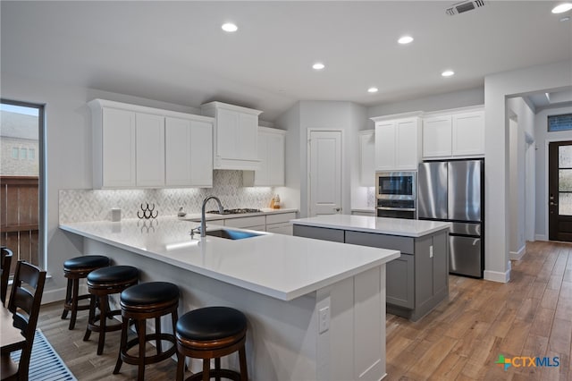 kitchen featuring light wood-style floors, light countertops, appliances with stainless steel finishes, a center island, and tasteful backsplash