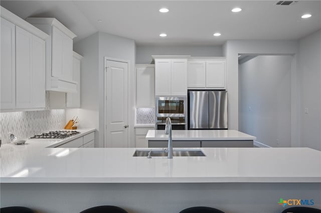 kitchen featuring a breakfast bar area, light countertops, decorative backsplash, appliances with stainless steel finishes, and a sink