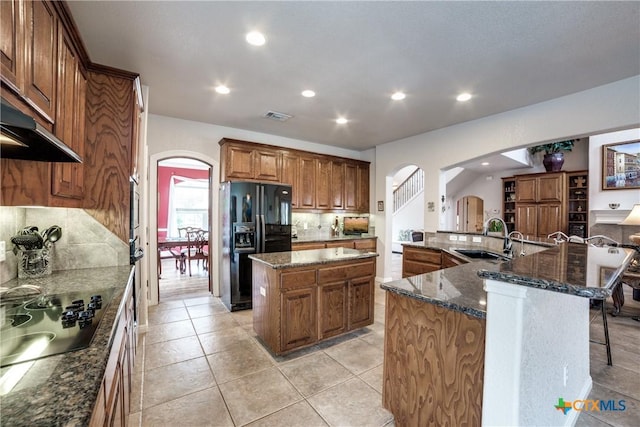 kitchen featuring a spacious island, sink, tasteful backsplash, dark stone counters, and black appliances