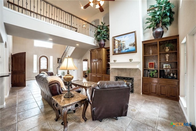 tiled living room featuring a tiled fireplace, a towering ceiling, and ceiling fan