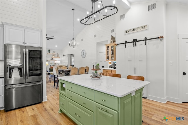 kitchen featuring stainless steel fridge, a barn door, white cabinets, and high vaulted ceiling