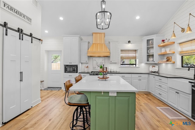 kitchen featuring white cabinetry, built in microwave, a barn door, decorative light fixtures, and custom exhaust hood