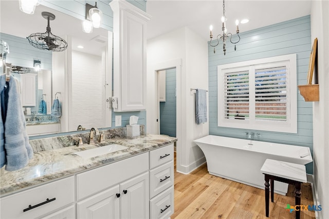 bathroom featuring vanity, wood-type flooring, a tub to relax in, and a chandelier