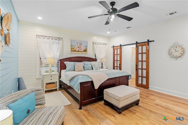 bedroom featuring a barn door, ceiling fan, and light wood-type flooring