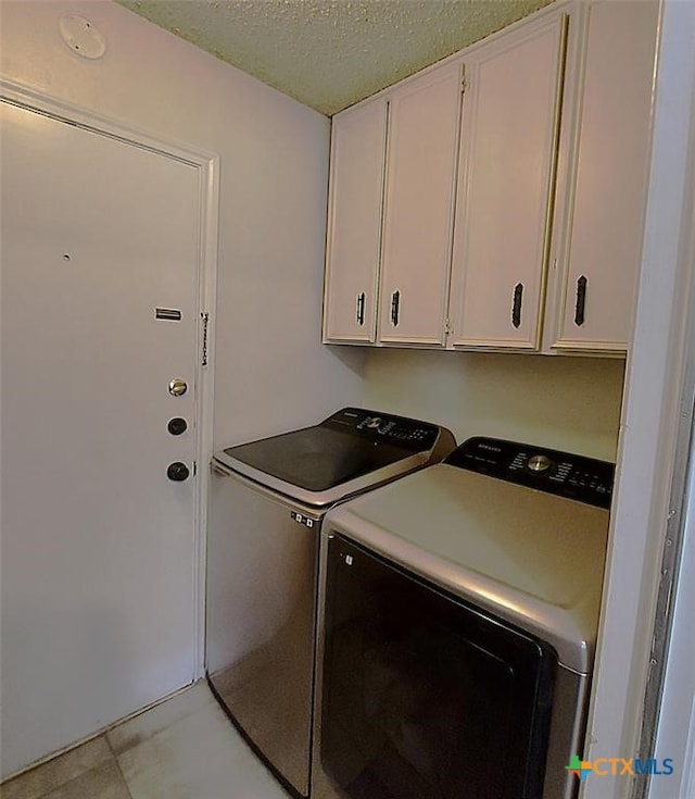 clothes washing area featuring a textured ceiling, cabinets, and washing machine and clothes dryer