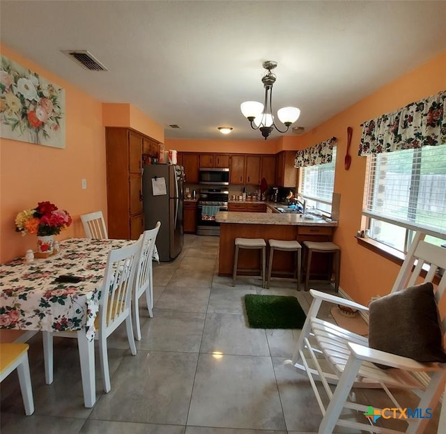 kitchen with appliances with stainless steel finishes, a notable chandelier, light tile patterned floors, hanging light fixtures, and kitchen peninsula