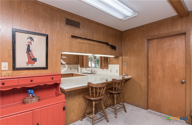 kitchen with wood walls, tile countertops, light carpet, and sink