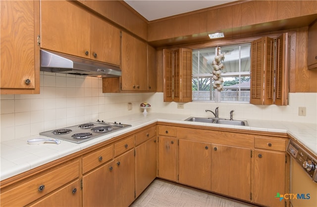 kitchen with tile countertops, dishwasher, stainless steel gas cooktop, sink, and tasteful backsplash