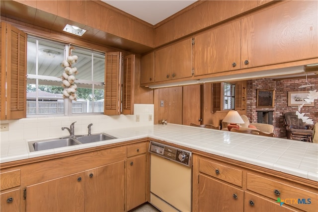 kitchen with tile counters, a brick fireplace, white dishwasher, decorative backsplash, and sink