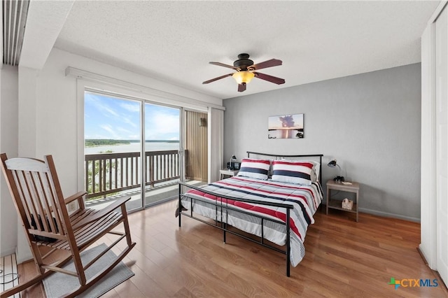 bedroom featuring a textured ceiling, wood finished floors, a ceiling fan, baseboards, and access to exterior