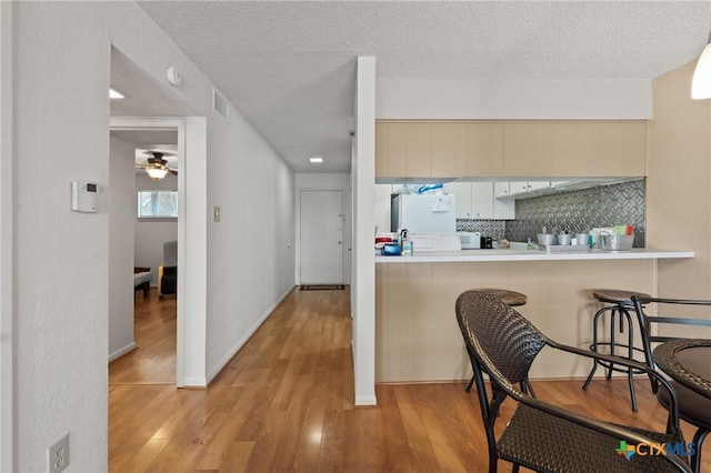 kitchen featuring decorative backsplash, a breakfast bar, wood finished floors, freestanding refrigerator, and a textured ceiling