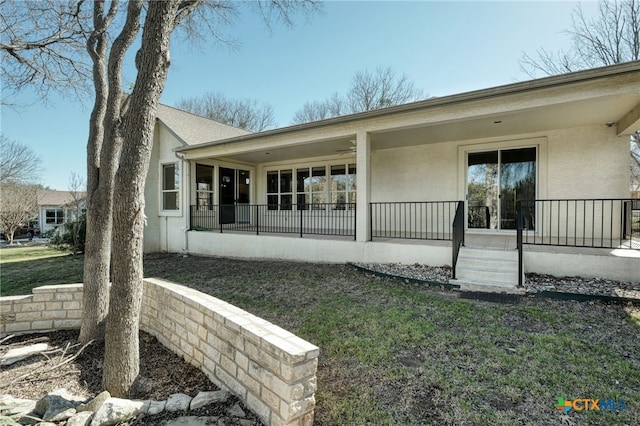 rear view of house featuring stucco siding, a yard, and covered porch