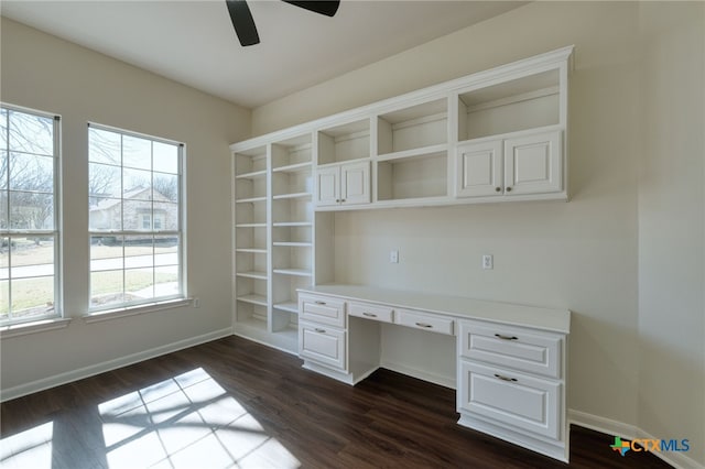 unfurnished office with dark wood-style floors, built in desk, a healthy amount of sunlight, and baseboards