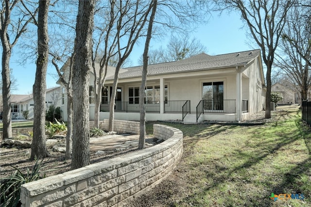 view of front facade featuring stucco siding, a porch, a front yard, and a shingled roof