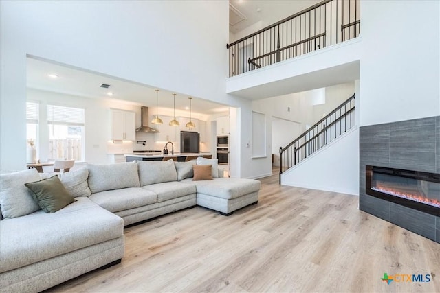 288 Smithsonian Ln, Kyle, TX 78640 - living room featuring stairway, a tile fireplace, a towering ceiling, light wood finished floors, and visible vents