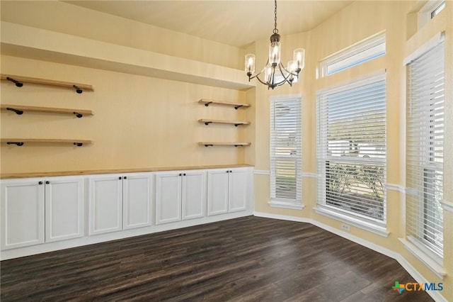 unfurnished dining area with dark wood-style floors, baseboards, and an inviting chandelier