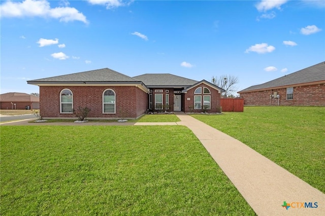 view of front facade featuring roof with shingles, a front yard, fence, and brick siding