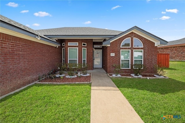 doorway to property featuring brick siding, a lawn, and roof with shingles