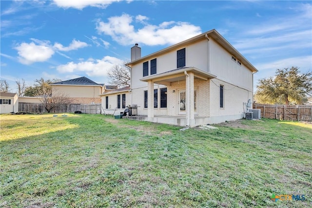 back of property featuring a yard, a fenced backyard, a chimney, and brick siding