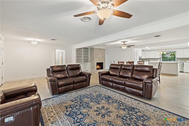 living area with visible vents, a fireplace, a ceiling fan, and ornamental molding