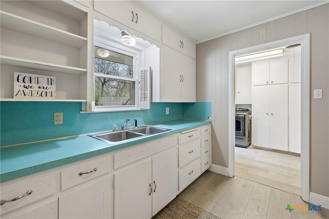 kitchen featuring crown molding, light countertops, light wood-style floors, white cabinets, and a sink