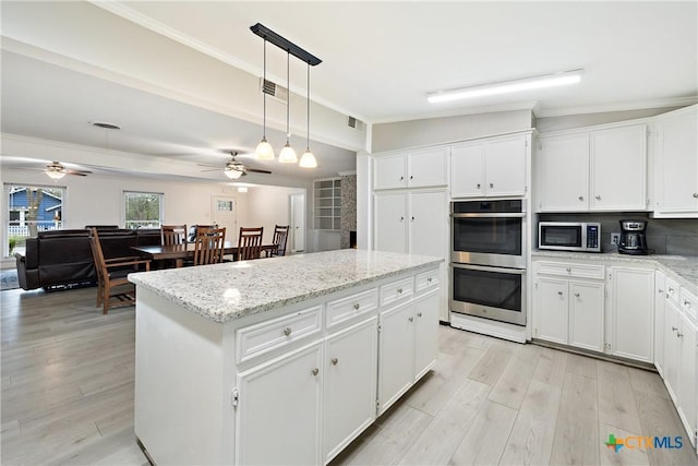 kitchen featuring light wood finished floors, a kitchen island, ceiling fan, ornamental molding, and appliances with stainless steel finishes