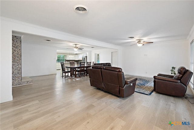 living room with visible vents, light wood-style flooring, crown molding, and ceiling fan