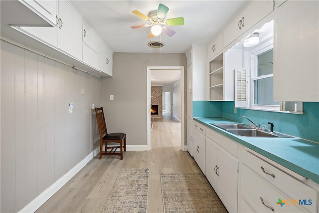 kitchen with light wood finished floors, visible vents, ceiling fan, white cabinetry, and a sink