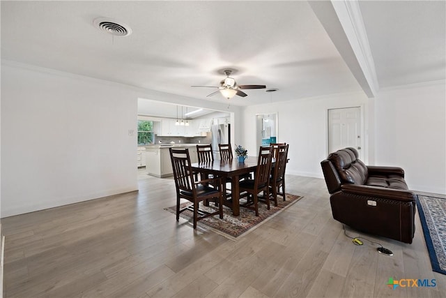 dining space featuring a ceiling fan, baseboards, visible vents, ornamental molding, and light wood-type flooring