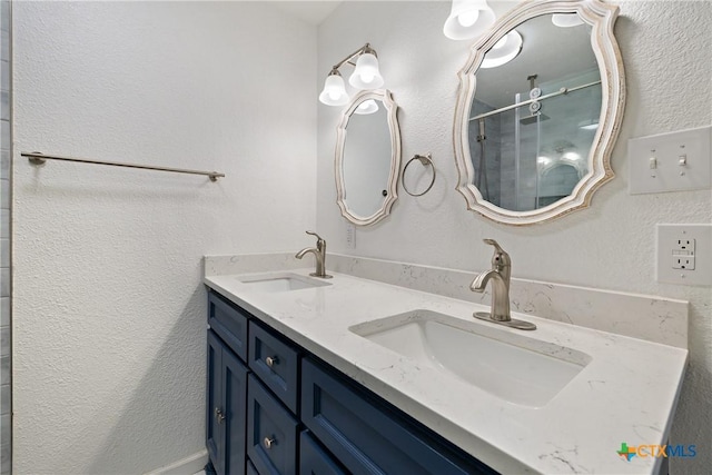 full bath with double vanity, a shower stall, a textured wall, and a sink