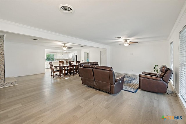 living area with crown molding, a ceiling fan, visible vents, and light wood finished floors