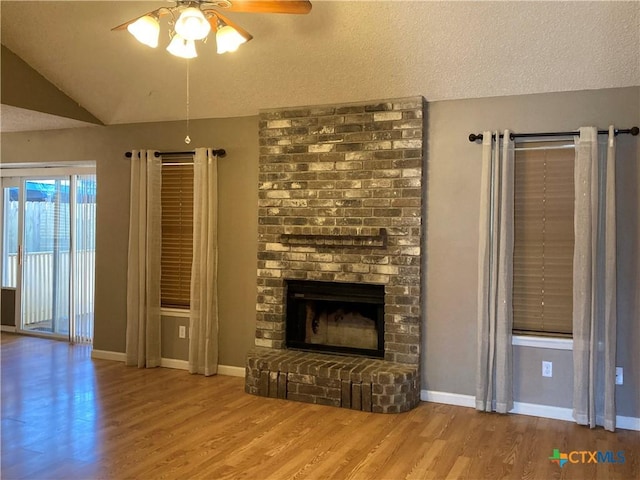 unfurnished living room featuring ceiling fan, a textured ceiling, vaulted ceiling, a fireplace, and hardwood / wood-style flooring