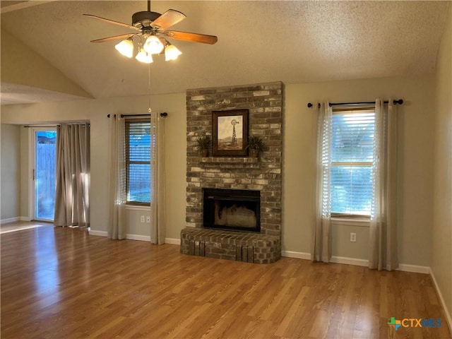 unfurnished living room with a brick fireplace, a textured ceiling, ceiling fan, wood-type flooring, and lofted ceiling