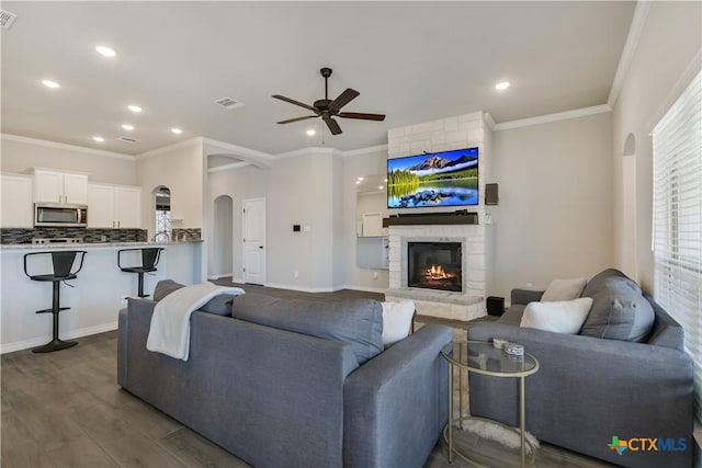 living room with a stone fireplace, ceiling fan, crown molding, and wood-type flooring