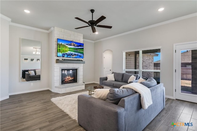 living room featuring a stone fireplace, ceiling fan, dark wood-type flooring, and ornamental molding