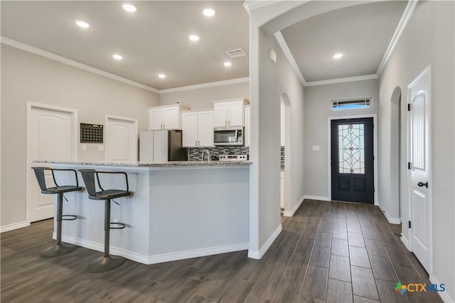 kitchen with white cabinetry, stainless steel appliances, a kitchen breakfast bar, light stone counters, and dark hardwood / wood-style flooring