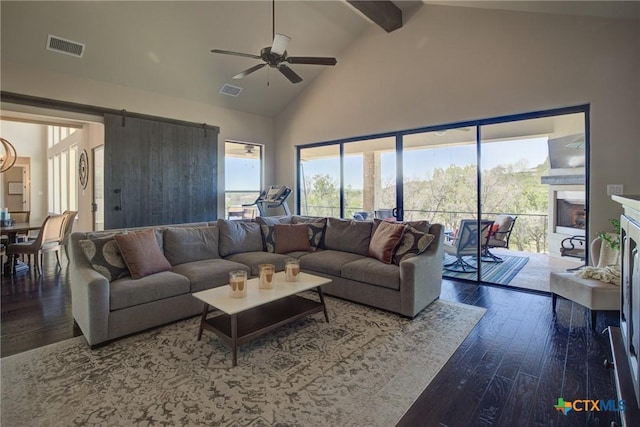 living room with a barn door, visible vents, hardwood / wood-style floors, a fireplace, and high vaulted ceiling