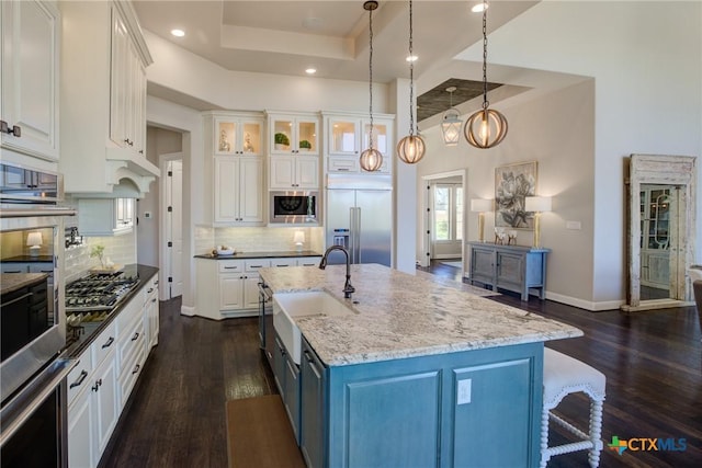 kitchen with white cabinets, a raised ceiling, dark wood-style flooring, built in appliances, and a sink