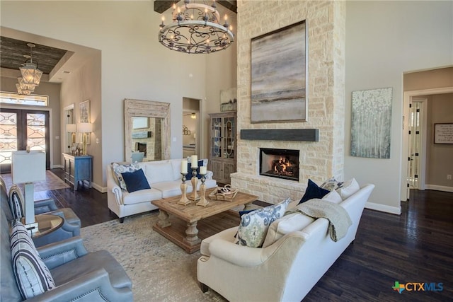 living area with a stone fireplace, wood finished floors, a towering ceiling, and an inviting chandelier