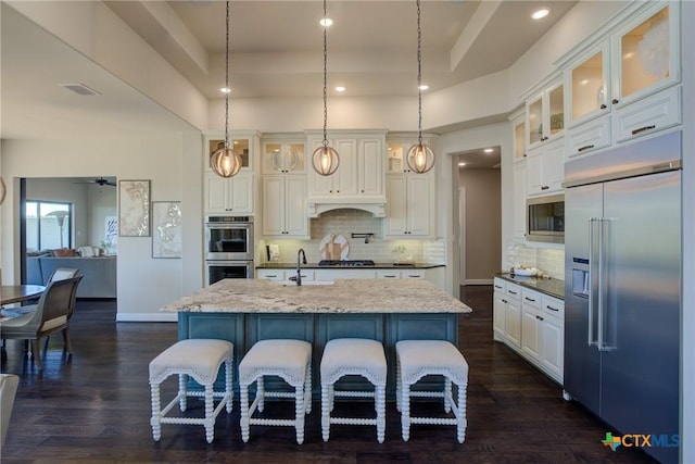 kitchen featuring a raised ceiling, visible vents, an island with sink, and built in appliances