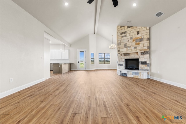 unfurnished living room with high vaulted ceiling, ceiling fan with notable chandelier, a stone fireplace, beamed ceiling, and light hardwood / wood-style floors